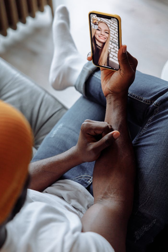 Black man relaxing on a couch during a video call on a smartphone, showcasing modern communication.